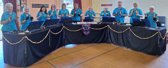 a group of people holding handbells and standing behind tables draped in black velvet